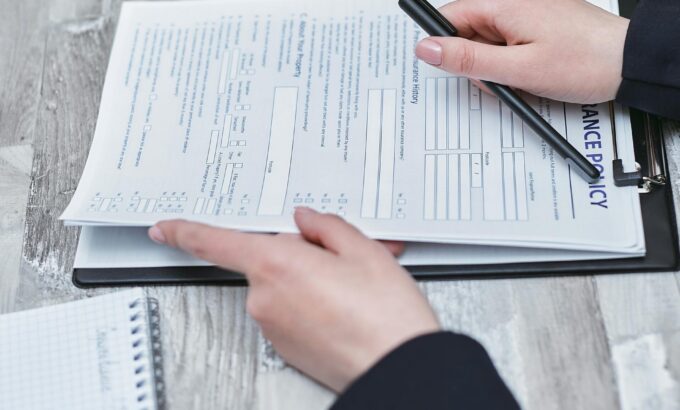 Free Close-up of hands analyzing insurance policy paperwork with pen on table. Stock Photo