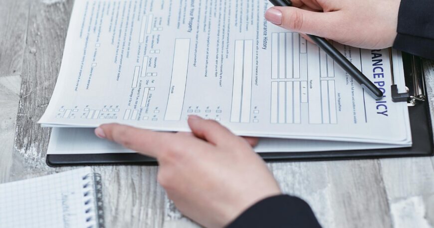 Free Close-up of hands analyzing insurance policy paperwork with pen on table. Stock Photo